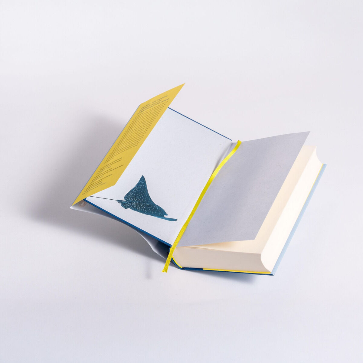 Ein aufgeschlagenes Buch mit einem gelben Umschlag und einem blauen Lesezeichen, auf einer weißen Oberfläche liegend. Die Seiten sind leicht abgewinkelt, was die Textur des Papiers zeigt.