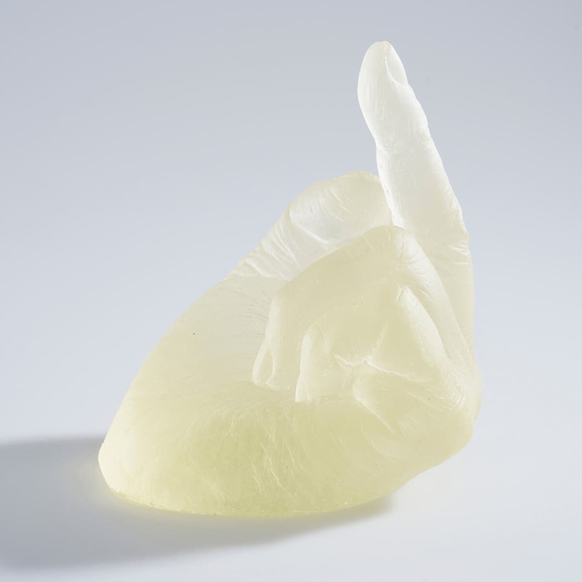 Eine Skulptur aus Glas mit dem Titel »Study of Perspective in Glass« von Ai Weiwei. Die Skulptur zeigt eine detailliert gearbeitete Hand, die eine Geste macht. Das Kunstwerk ist hauptsächlich elfenbeinfarben und transluzent, mit weißen Akzenten, und steht auf einer glatten, neutralen Oberfläche.