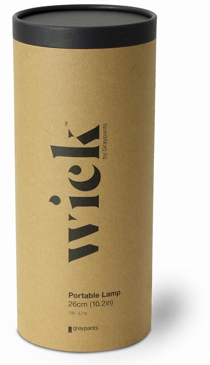Eine Wick Tischlampe in einer braunen Pappverpackung mit schwarzem Deckel. Die Verpackung zeigt die Beschriftung 'Wick' und andere Details in schwarzer Farbe.