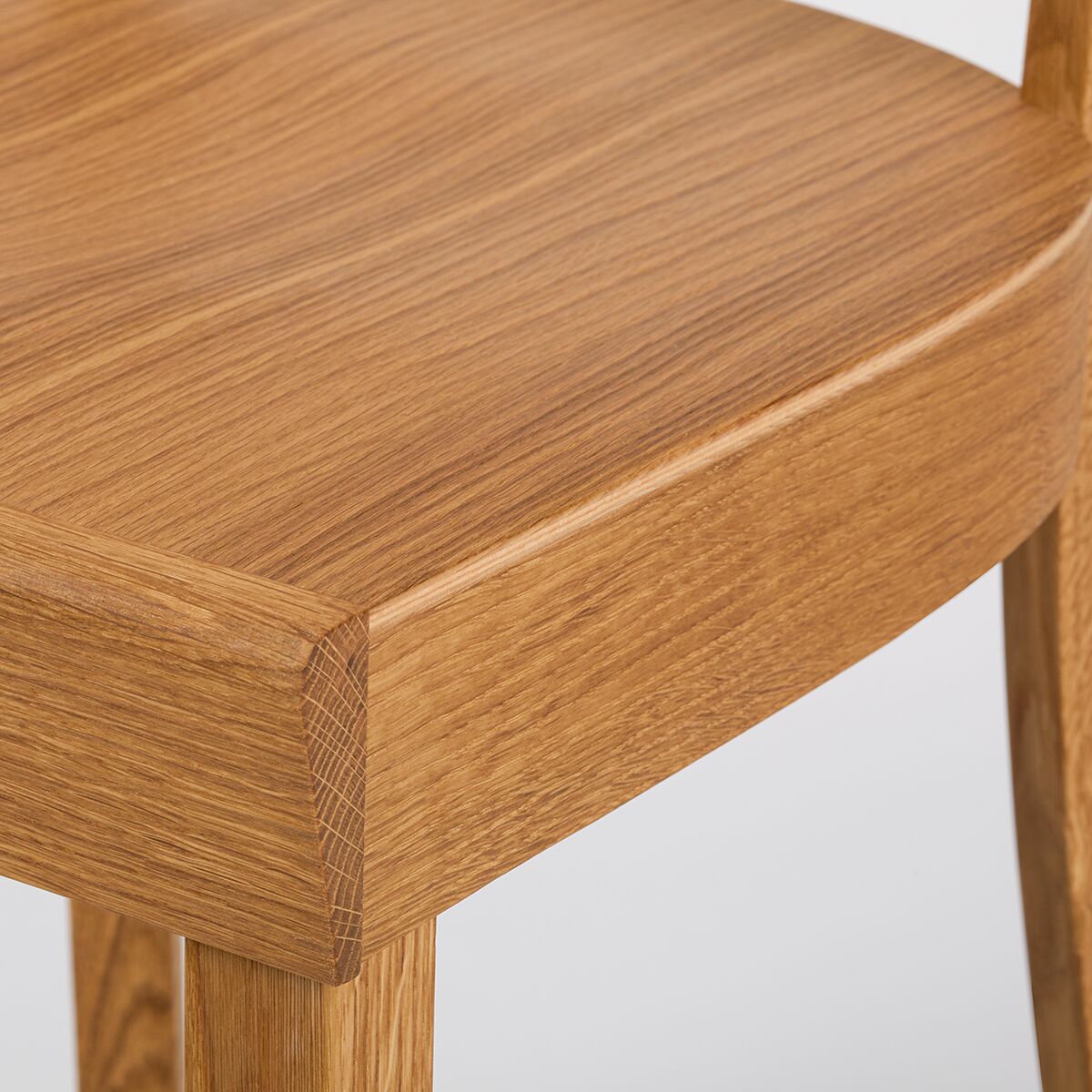 Detailaufnahme eines Frankfurter Küchenstuhls der ZEIT Sonderedition aus geölter Eiche. Sichtbar sind Sitzfläche und Beine aus hellem Massivholz auf neutralem Hintergrund. Der Stuhl zeigt feine Holzmaserung und hochwertige Verarbeitung.