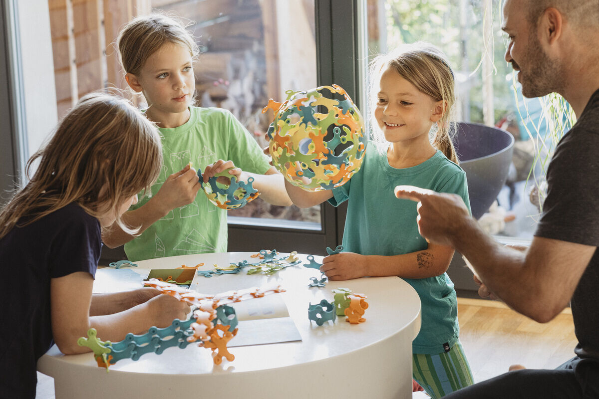 Vier Kinder sitzen an einem runden Tisch und spielen mit Binabo, einem bunten Steckspielzeug bestehend aus verschiedenen Formen und Farben.