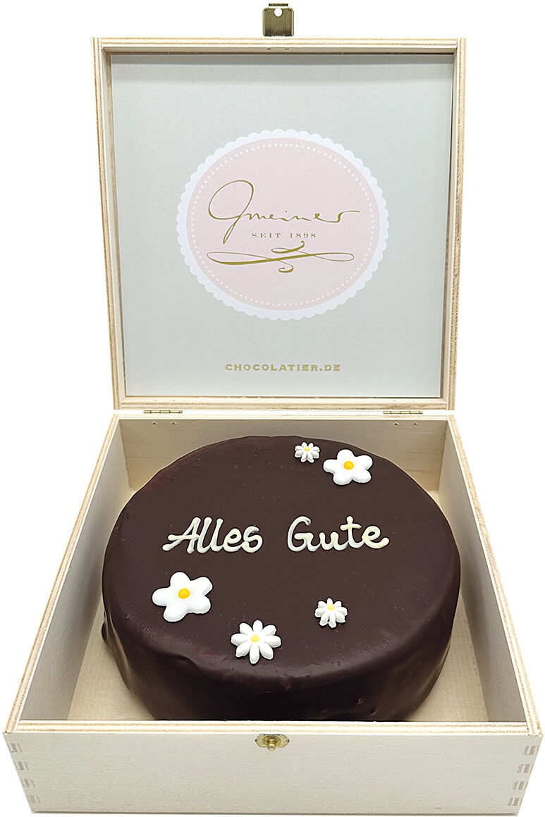Eine luxuriöse Sachertorte in einer eleganten Geschenkbox mit der Aufschrift 'Alles Gute', garniert mit stilisierten weißen Blüten.