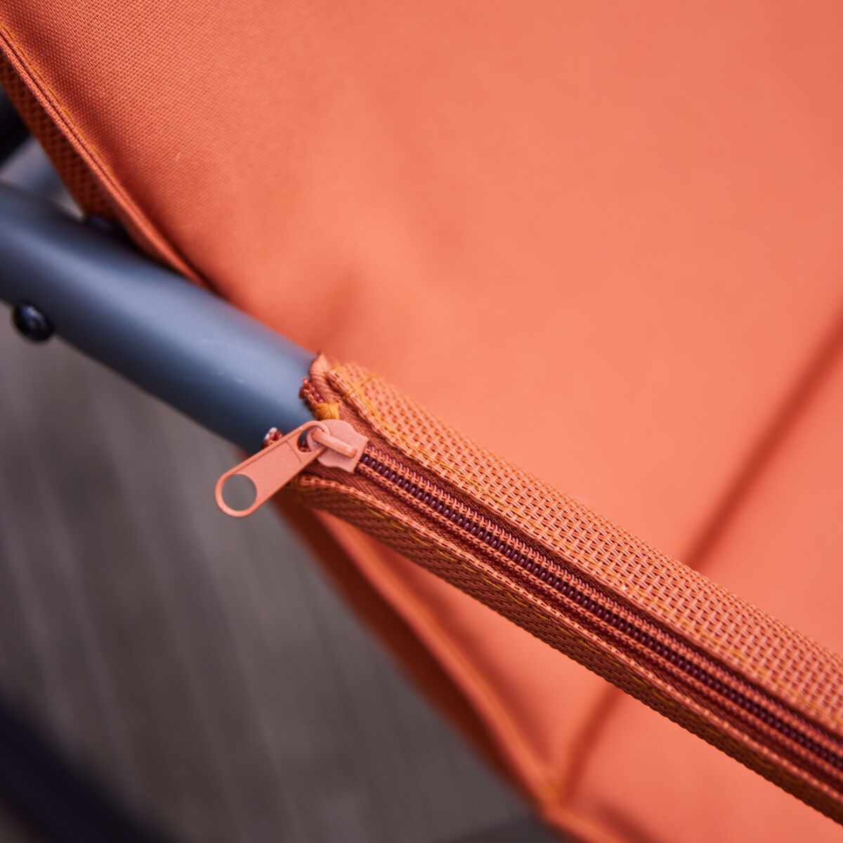 Nahaufnahme einer orangen Swingliege »Aliano« mit sichtbarem Reißverschluss und dunkelgrauem Metallgestell, geeignet für Nutzung im Garten oder auf der Terrasse.
