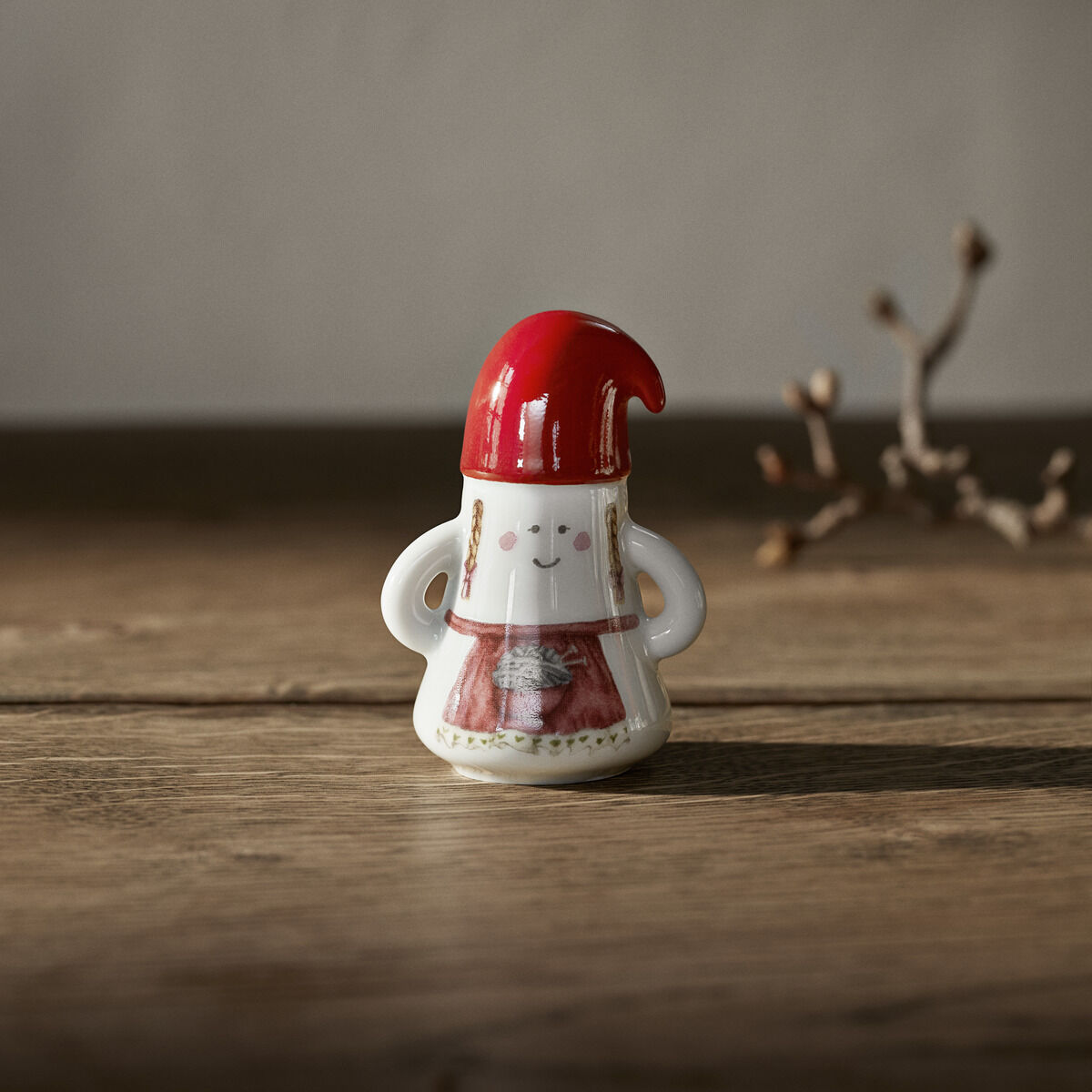 Keramikfigur einer stilisierten Weihnachtsfrau »Hammershøi« mit roter Mütze und weiß-rotem Kleid, stehend auf einem Holztisch mit dezentem winterlichem Hintergrund.