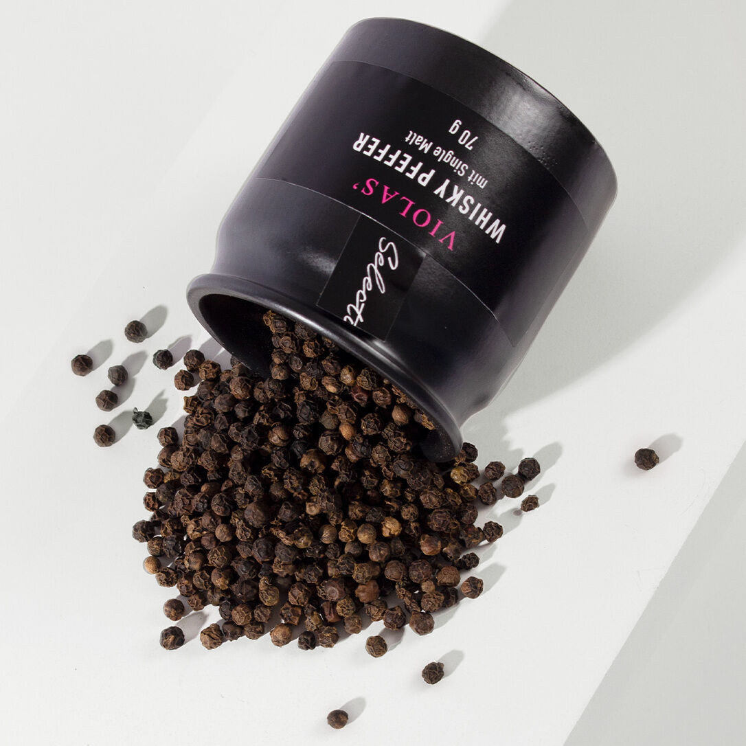 Eine schwarze Dose mit der Aufschrift 'Whisky Pfeffer' liegt auf der Seite und schwarzer Pfeffer ist herausgefallen. Die Dose gehört zur ZEIT Genuss-Selection.