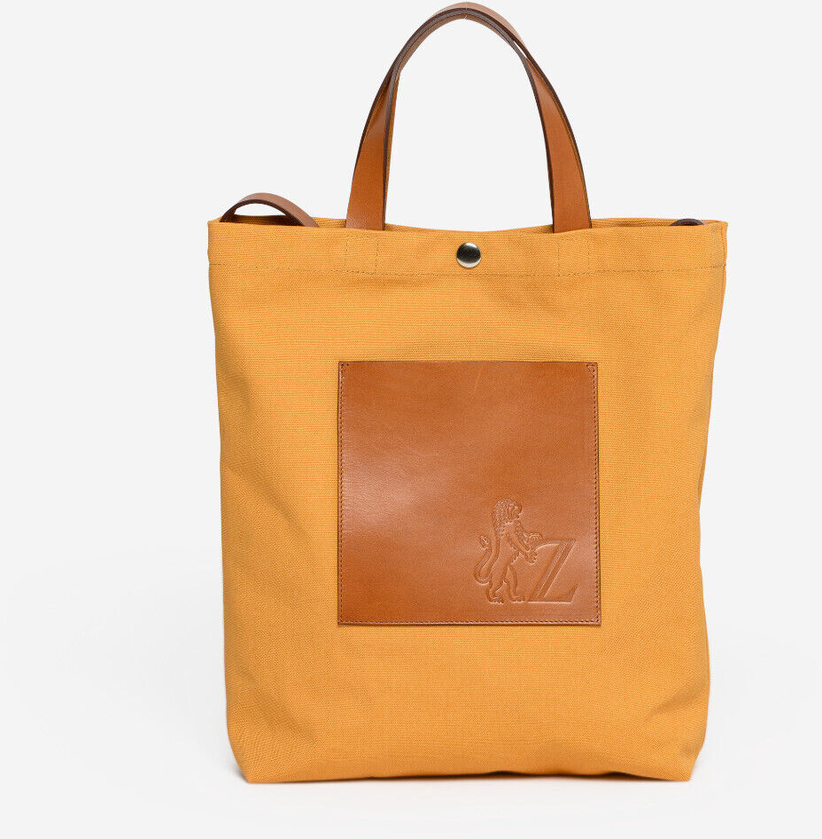 Dies ist eine stilvolle und praktische Einkaufstasche, der ZEIT Shop Jubiläums-Shopper. Die Tasche besteht aus gelbem Stoff und hat braune Lederapplikationen. Sie hat kurze Henkel und eine lederne Tasche vorne in der Mitte. Sie eignet sich für den täglichen Gebrauch und als feines Geschenk.