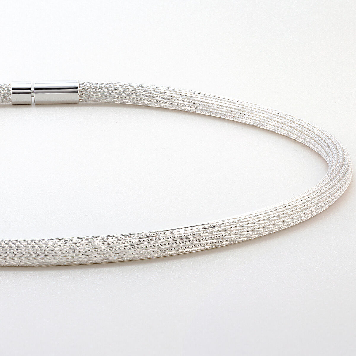 Das Bild zeigt das Collier »Milanaise« von Menard, ein handgefertigtes Schmuckstück aus feinen Silberdrähten. Die Oberfläche ist glatt und das Geflecht rund, mit einem silberfarbenen Verschluss. Es wirkt edel und modern auf einem hellen Hintergrund.
