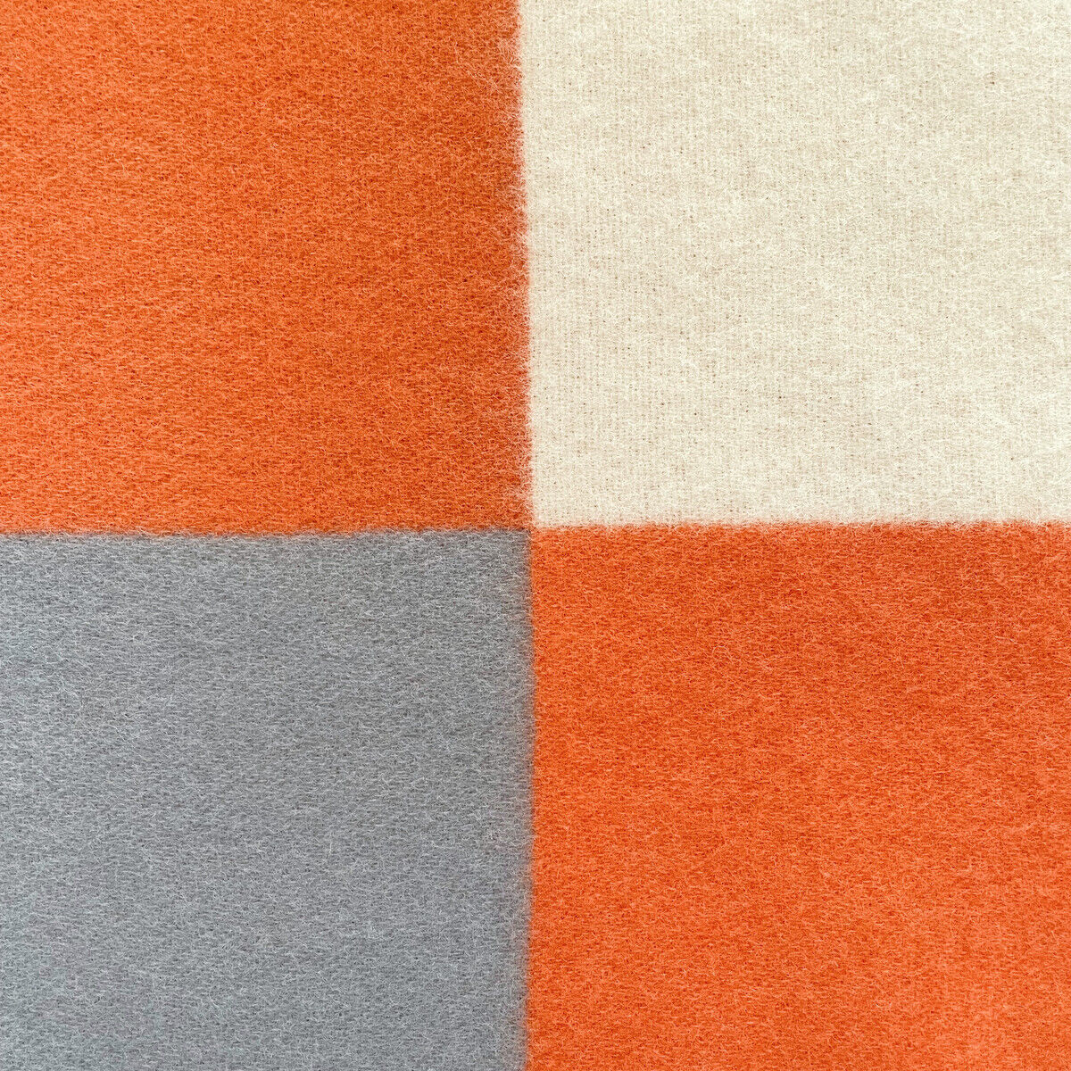 Eine Decke mit einem tricolor Design bestehend aus orangefarbenen, weißen und grauen Quadraten, geeignet als gemütliches Wohnaccessoire.