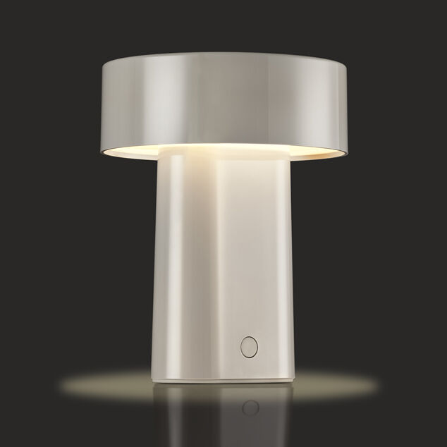 Auf dem Bild ist eine moderne, tragbare Tischlampe mit weißem, minimalistischem Design auf dunklem Hintergrund zu sehen. Die Lampe hat einen breiten, runden Schirm und ein rechteckiges Gehäuse. Das warmweiße Licht schafft eine gemütliche Atmosphäre. Die Lampe ist eingeschaltet und wirft einen sanften Lichtschein auf den Untergrund.