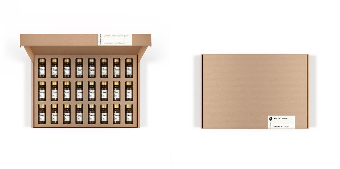 Eine geöffnete Adventskalender Tastingbox mit 24 kleinen Flaschen, sowie eine geschlossene Box, beide in brauner Farbe. Jede Flasche scheint versiegelt zu sein und die Box ist schlicht mit einem weißen Etikett dekoriert.