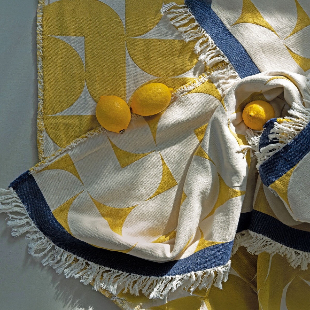 Die Baumwolldecke »Stockholm« von Eagle Products liegt dekorativ auf einem modernen Sofa. Sie zeigt ein geometrisches Muster in Gelb und Weiß mit Fransen und farbiger Bordüre. Die Szenerie betont Gemütlichkeit und skandinavisches Design in hellen Räumen.