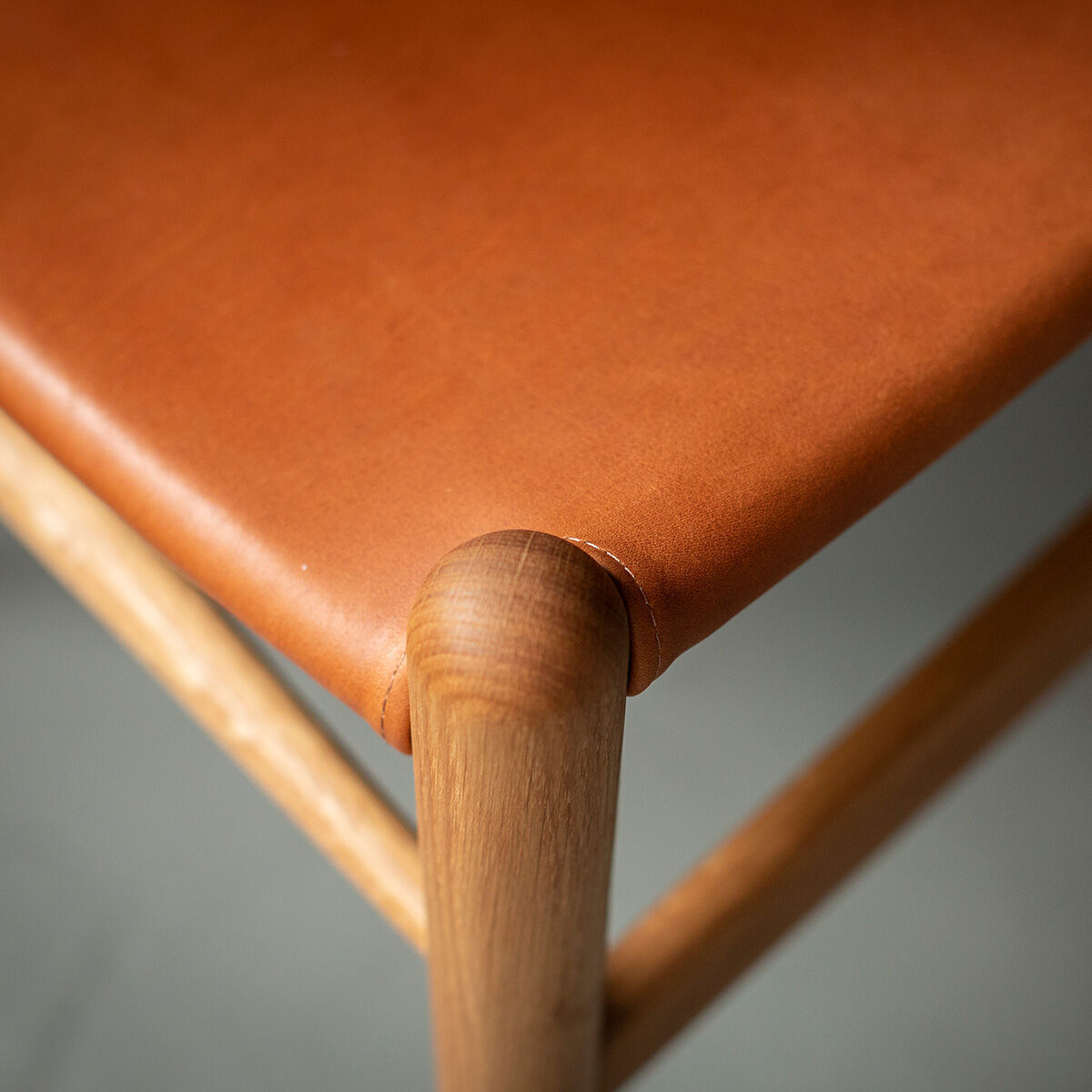 Nahaufnahme eines ZEIT Sonderedition »CH24« Wishbone Chairs aus Eiche und Leder. Der Sitz ist aus braunem Leder und das Gestell aus hellem Naturholz gefertigt.