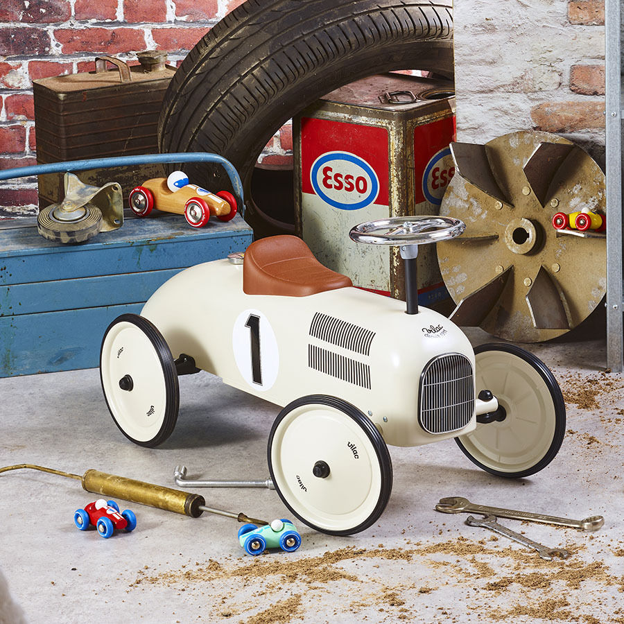 Weißes Vintage-Tretfahrzeug für Kinder in einer mechanischen Werkstatt Umgebung, umgeben von Reifen und Werkzeugen, mit Essenz-Behältern im Hintergrund.