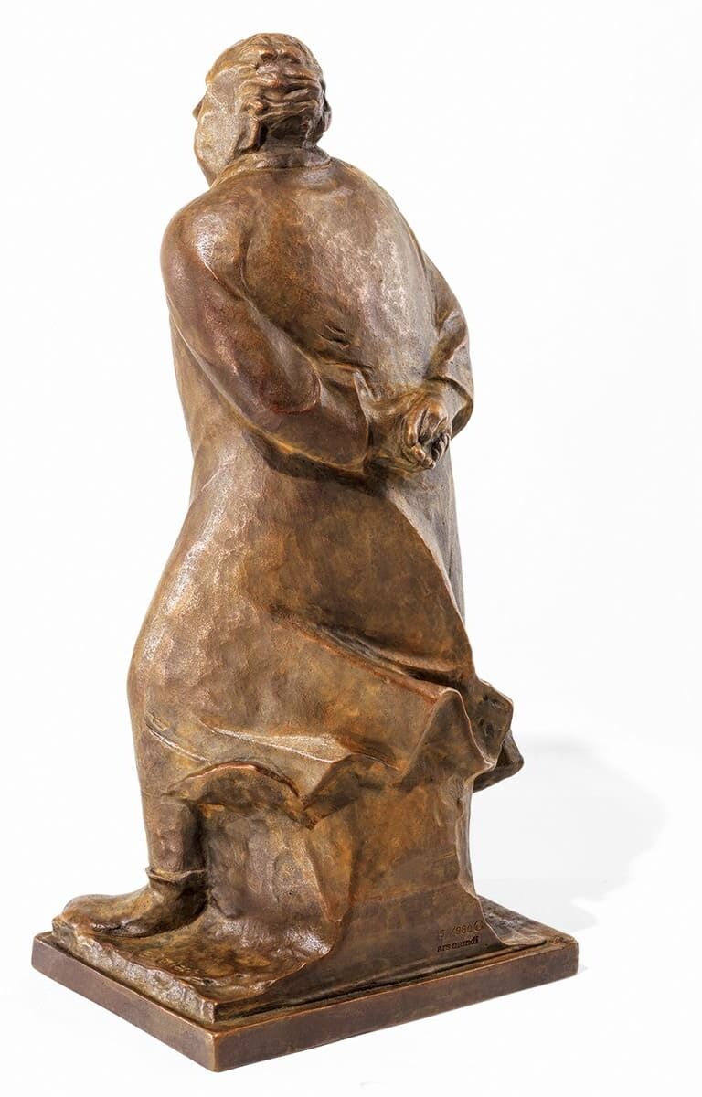 Eine Skulptur von Ernst Barlach mit dem Titel »Der Spaziergänger«. Die Bronzeskulptur zeigt eine stehende Figur, die nach hinten gewandt ist und die Hände auf dem Rücken verschränkt hält. Die Figur trägt einen langen Mantel und steht auf einer rechteckigen Basis.