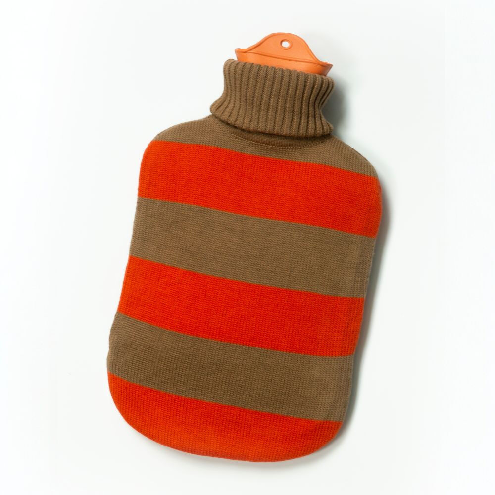Schräg auf weißem Grund liegende SUITE702 Wärmflasche »gestreift« mit weichem, grob geripptem Strickbezug. Der Bezug zeigt breite horizontale Streifen in leuchtendem Rot und warmem Braun sowie einen hohen braunen Rollkragen. Oben ragt der orangefarbene Verschluss mit kleiner weißer Öffnung heraus.