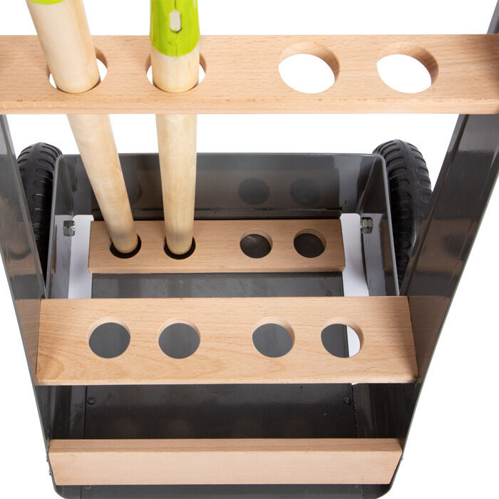 Ein Gartentrolley mit einem Werkzeug-Set für Kinder, bestehend aus Holzstangen und grünen Werkzeuggriffen, montiert auf schwarzen Rädern.