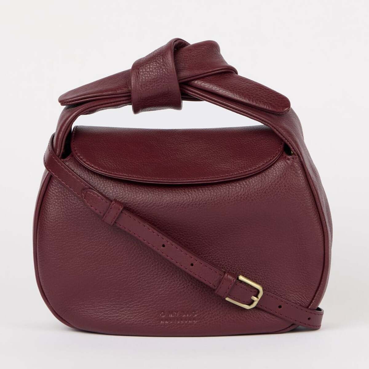 Abgebildet ist eine elegante Umhängetasche aus bordeauxfarbenem Leder mit Überschlag und verstellbarem Schulterriemen. Die Tasche trägt den Namen »Coco Croissant« und ist auf einem hellen, neutralen Hintergrund zu sehen. Das Design ist minimalistisch und modern, mit goldfarbener Schnalle am Riemen.