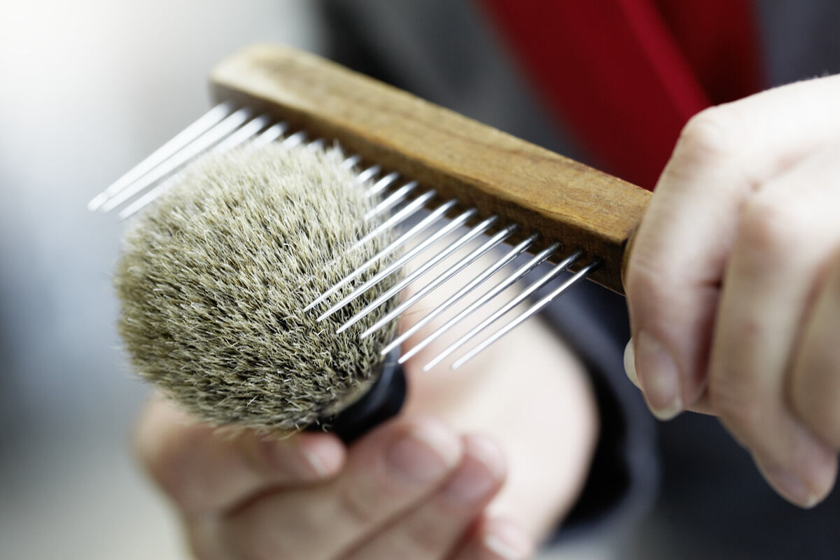 Eine Nahaufnahme eines Rasiersets mit einem Rasierpinsel aus feinem Dachshaar und einem Holzgriff, der neben einem Kamm gezeigt wird.