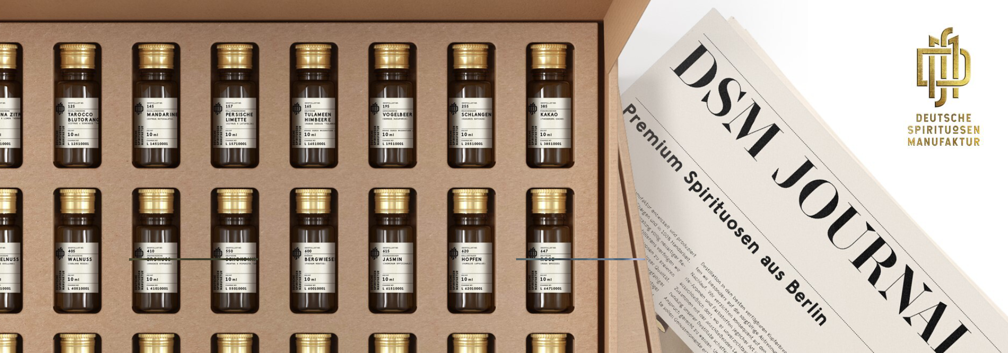 Reihe von kleinen Spirituosenflaschen mit goldenen Kappen in einer Geschenkbox neben einer Ausgabe des DSM Journals und dem Logo der Deutschen Spirituosen Manufaktur