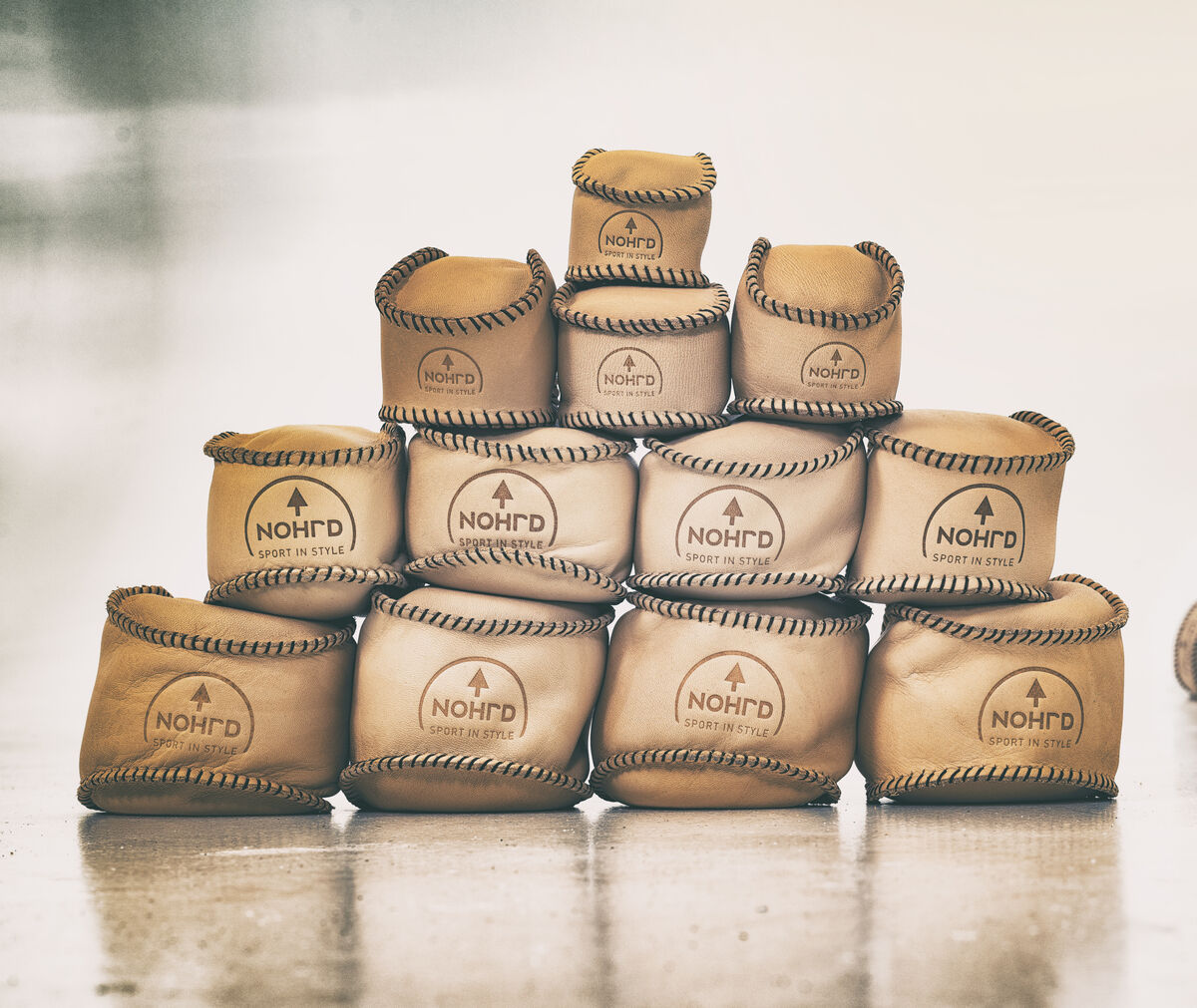 Das Bild zeigt eine Pyramide aus naturfarbenen HaptikBällen, die auf dem Boden gestapelt sind. Einige Bälle sind verstreut auf der rechten Seite. Die Bälle haben ins Auge fallende Nähte und eine strukturierte Oberfläche, die auf hochwertige Handwerkskunst hinweisen.