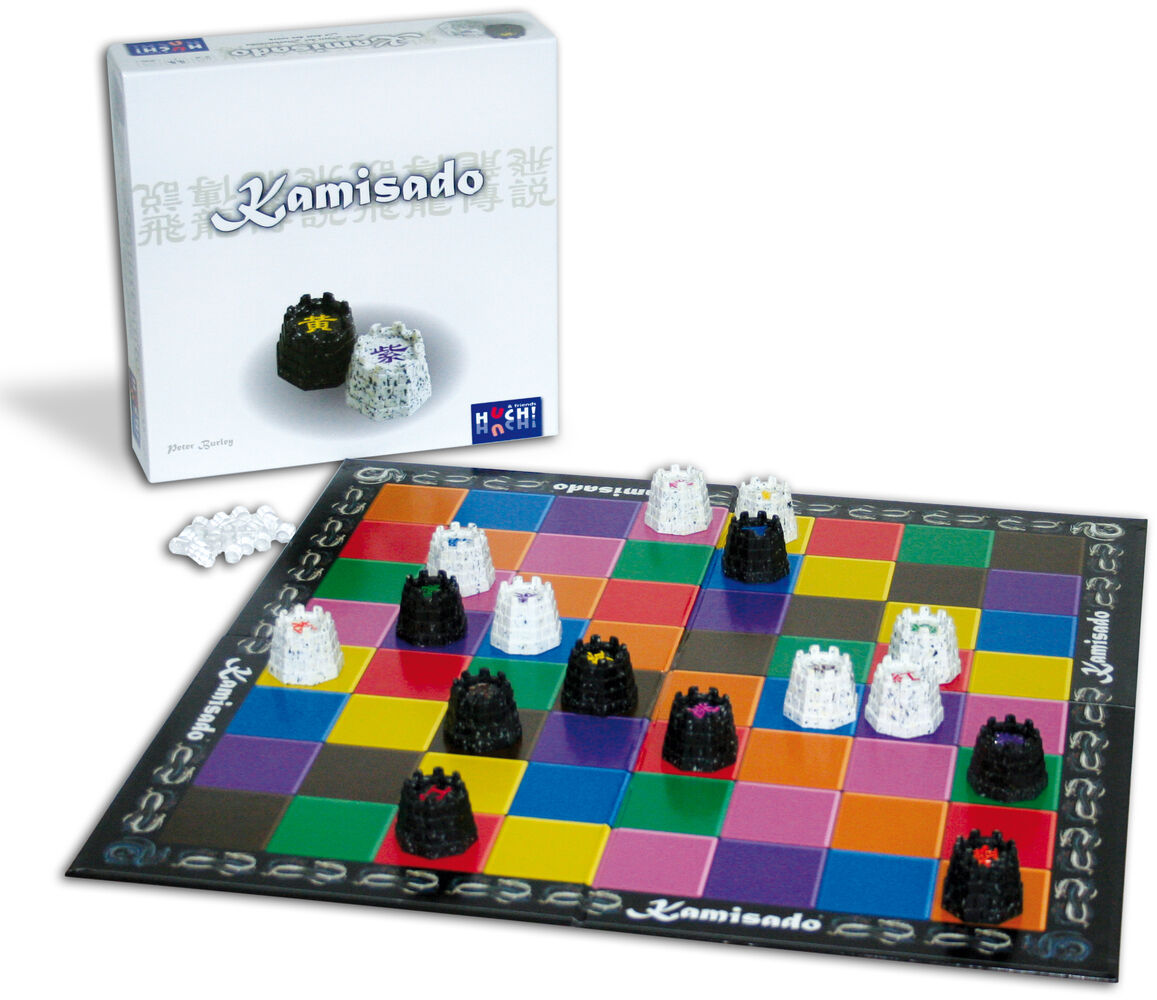 Ein Bild des Brettspiels 'Kamisado' zeigt ein quadratisches Spielbrett mit bunten Feldern und schwarzen und weißen Figuren, die Drachen darstellen. Im Hintergrund ist die Verpackung des Spiels zu sehen.