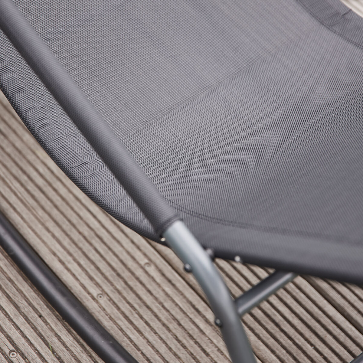 Detailaufnahme einer modernen grauen Swingliege »Aliano« aus Metall und Netzstoff, platziert auf einer Holzterrasse. Die Liege ist ergonomisch geformt und eignet sich für entspanntes Sitzen im Freien.