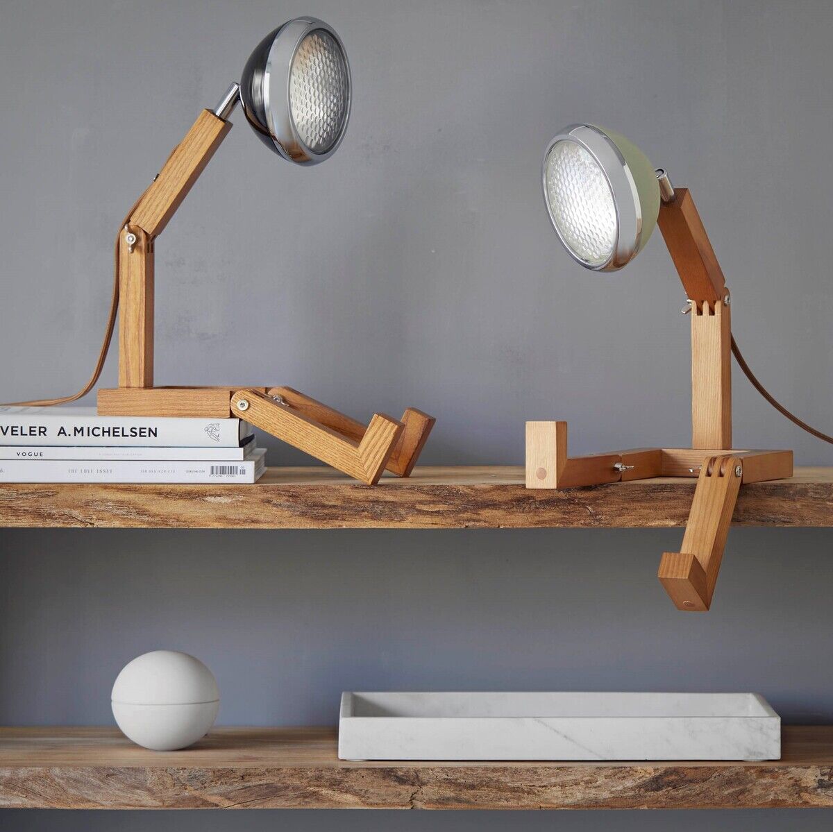 Zwei Tischlampen der Marke 'Mr. Wattson' auf einem Holzregal, die teilweise aus Holz und Metall bestehen. Eine Lampe steht aufrecht, während die andere hingesetzt ist. Sie haben einen retro-modernen Designstil.