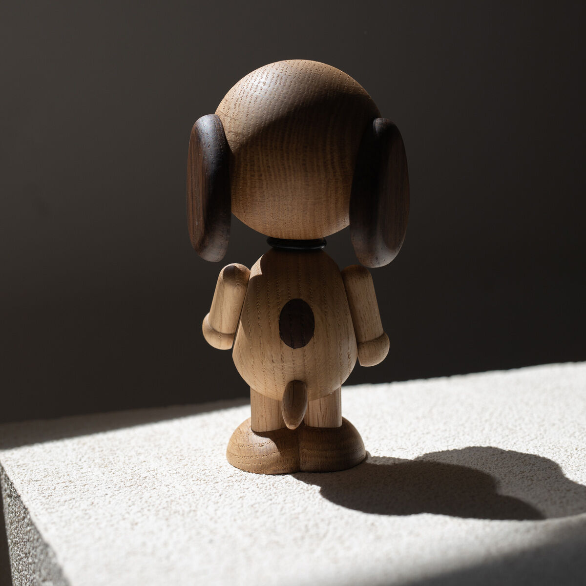 Holzfigur »Snoopy« aus der Sicht von hinten. Die Figur steht auf einer hellen Oberfläche, präsentiert eine schlichte Holzverarbeitung und zeigt dunkle Ohren.