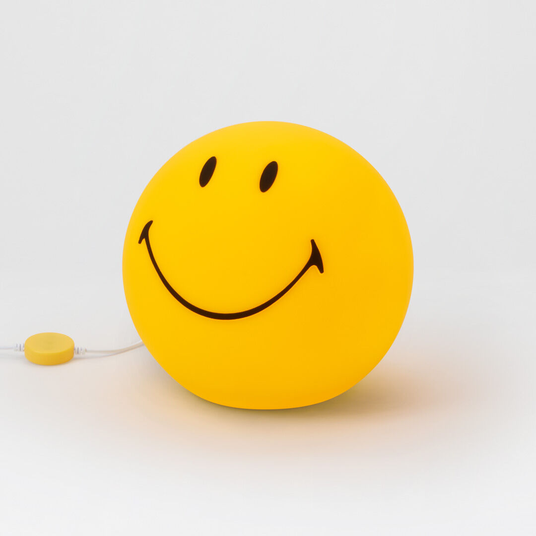 Die Abbildung zeigt eine runde, gelbe LED-Lampe in Form eines großen Smiley-Gesichts mit schwarzen Augen und breitem Mund auf weißem Hintergrund. Das Kabel mit Schalter ist am unteren linken Rand zu sehen.