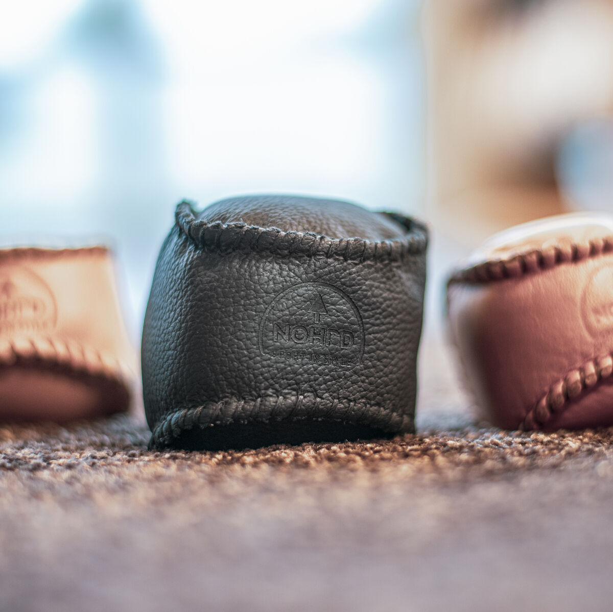Drei HaptikBälle »Schwarz«, ein schwarzer, ein brauner und ein beiger, aus Lederoptik-Material auf einem Teppich liegend, verschwommener Hintergrund.