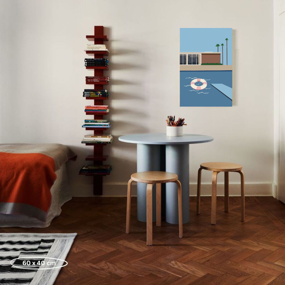 Ein modern eingerichtetes Wohnzimmer mit einem Malen nach Zahlen Bild an der Wand. Das Bild zeigt ein minimalistisches Pool-Szenario mit hellblauem Wasser, einem orangefarbenen Rettungsring und einer beigen Wand im Hintergrund. Auf dem runden Tisch in der Mitte sind Farbstifte und ein unvollendetes Gemälde vorbereitet. Rechts stehen zwei Holzstühle, und links ist ein Sessel mit einer orangefarbenen Decke. Ein Regal mit Büchern befindet sich an der linken Wand.