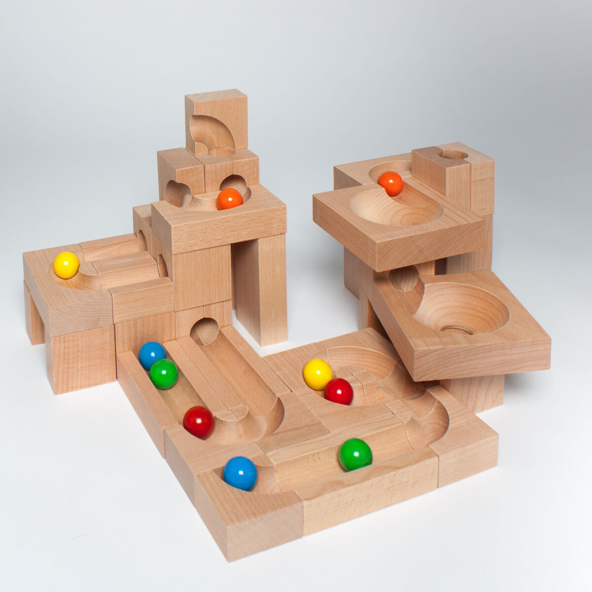 Eine modulare Holz-Kugelbahn bestehend aus mehreren Bauteilen mit bunten Kugeln in Rot, Blau, Gelb und Grün, die für Kinder ein kreatives und pädagogisches Spielerlebnis bietet.