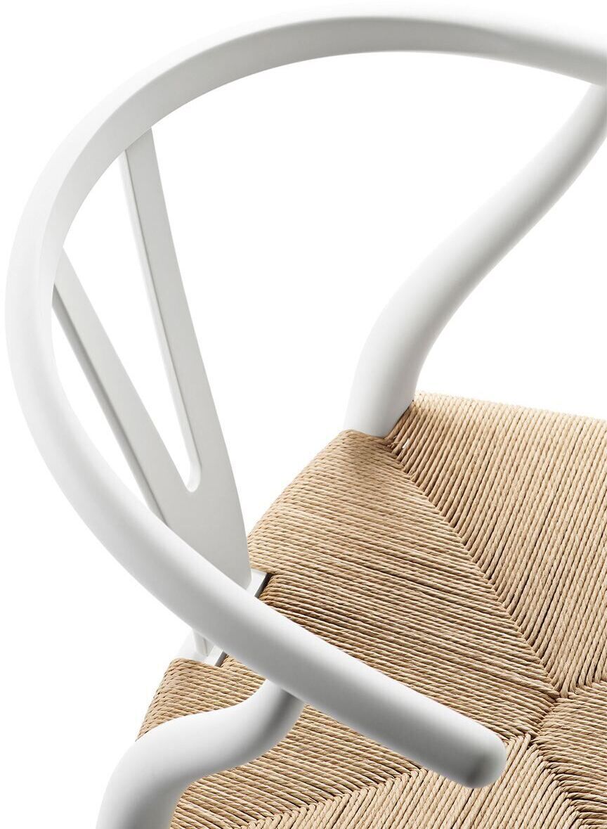 Nahaufnahme eines CH24 Soft Stuhls von Carl Hansen. Der Stuhl hat eine geschwungene Rückenlehne und eine geflochtene Sitzfläche in Naturfarben. Die Struktur des Stuhls ist weiß.