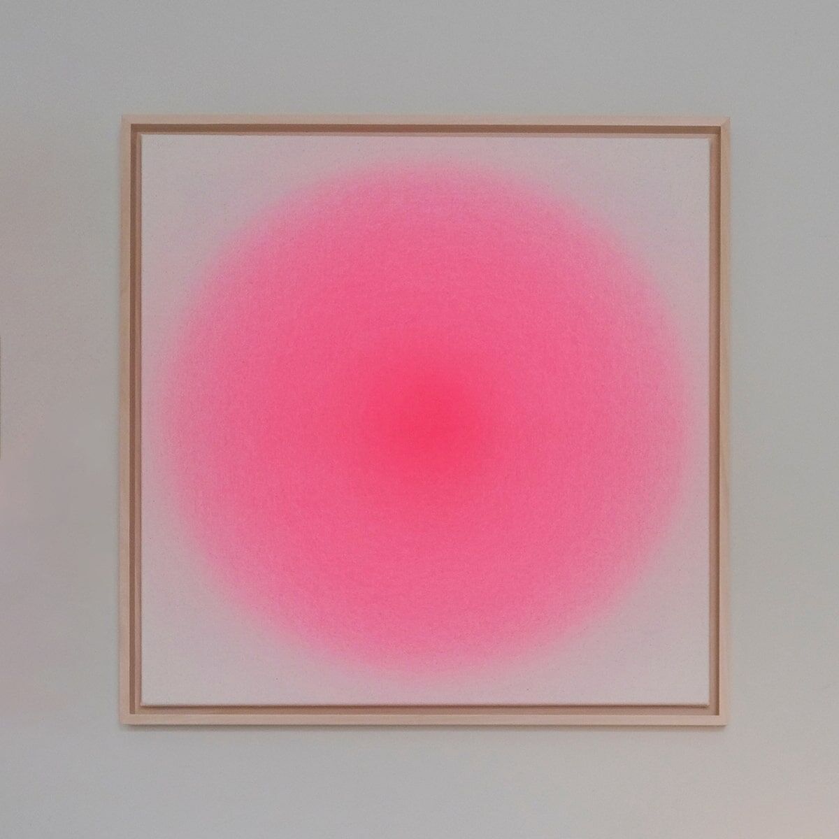 Ein quadratisches Kunstwerk in einem Holzrahmen zeigt einen sanften Farbverlauf von kräftigem Pink in der Mitte zu Weiß an den Rändern.