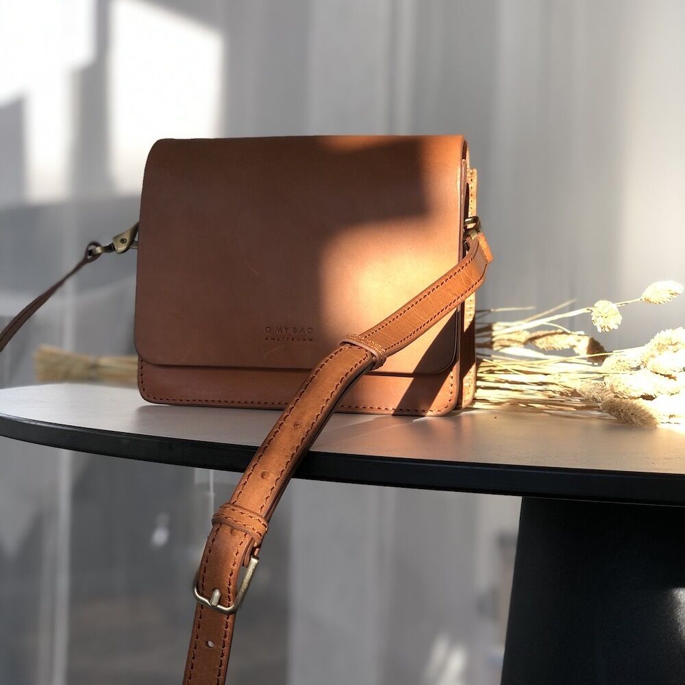 Eine stilvolle Umhängetasche aus Apfelleder, Modell »Audrey Mini«, in elegantem Braun und natürlichen Farbtönen, auf einem modernen runden Tisch inszeniert.