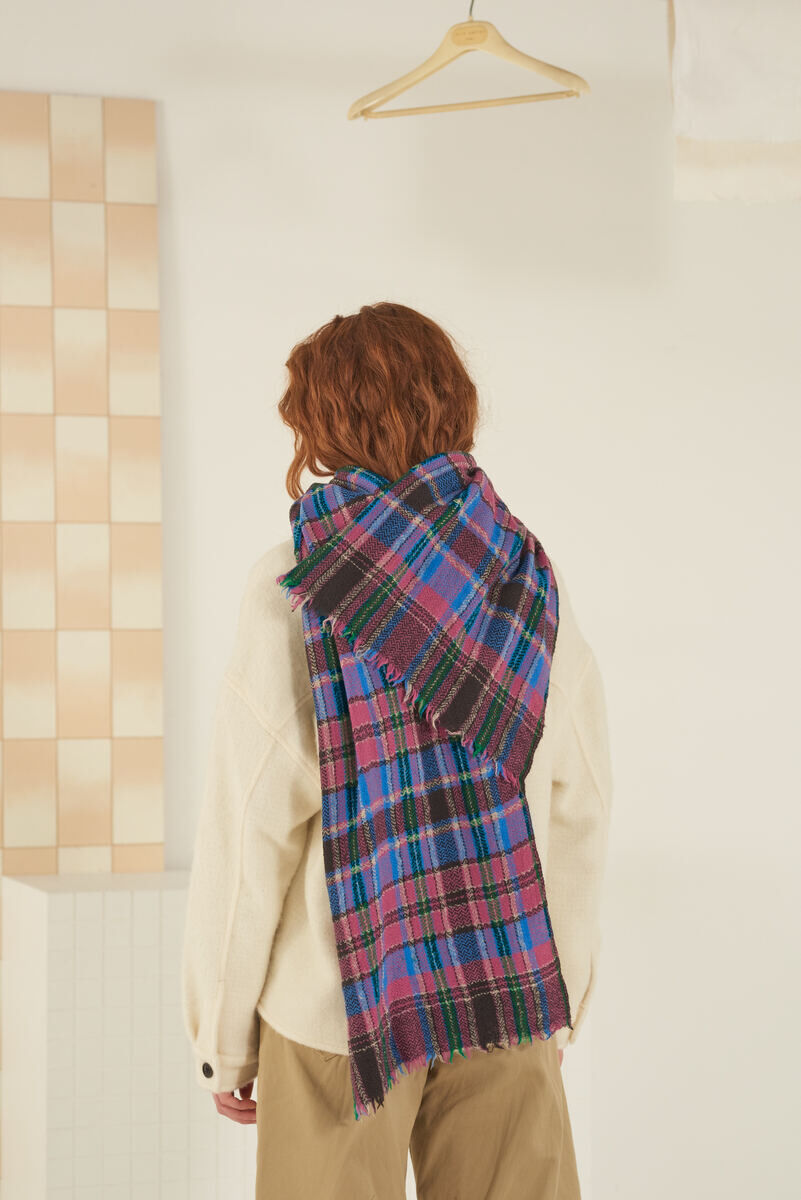 Eine Person mit rotem Haar trägt einen karomustigen Schal in Charcoal über einer weißen Jacke. Der Schal hat Farben wie Grau, Rot, Blau und Schwarz.