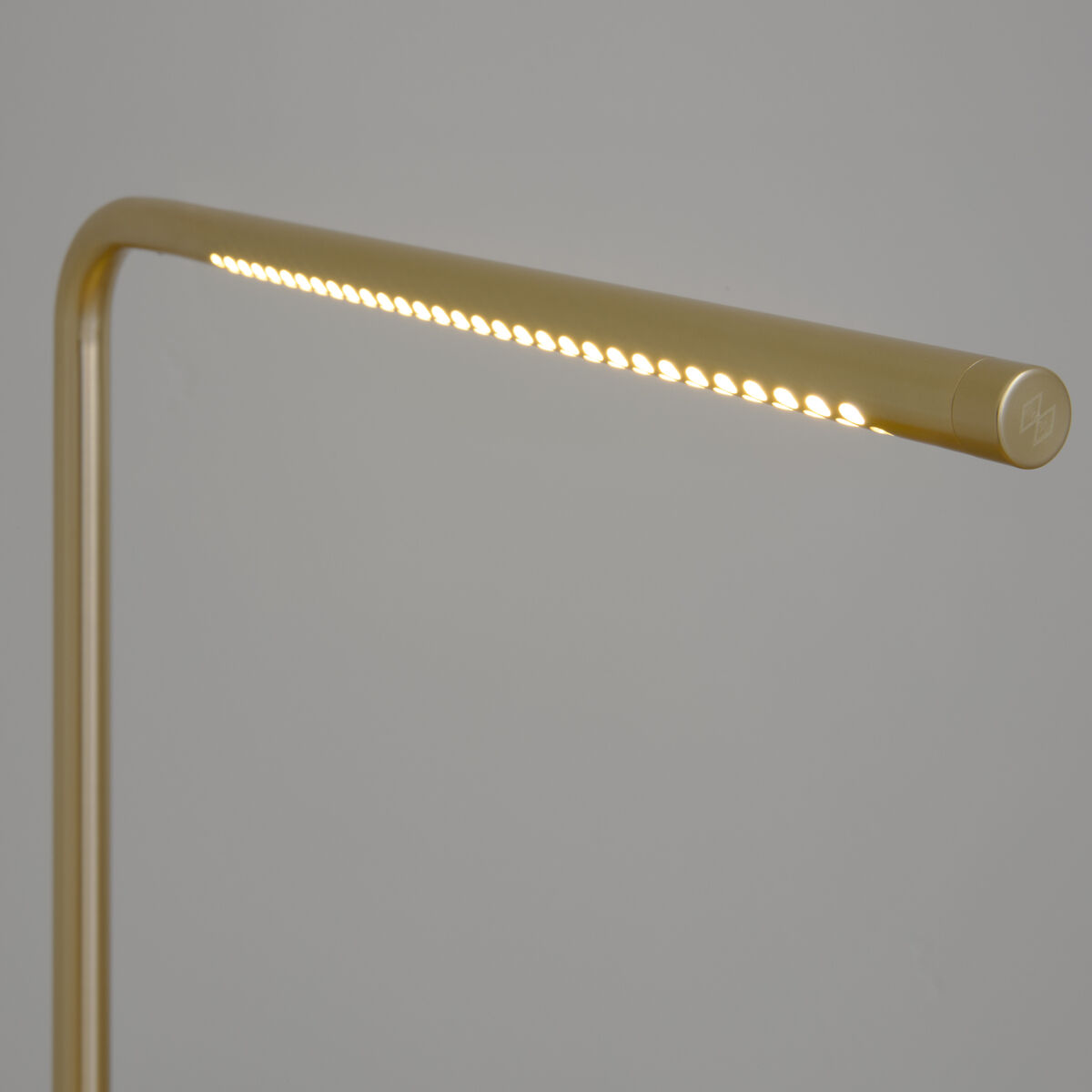 Detailansicht der Stehleuchte »Omni« von Umage in Gold. Zu sehen ist der schmale, rechteckig gebogene Leuchtenarm mit integrierten, warmweiß leuchtenden LEDs. Das Design wirkt modern und minimalistisch vor neutral-grauem Hintergrund.