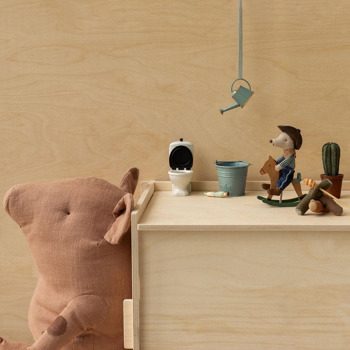 Spielzeug-Arrangement mit Cowboy-Maus auf einem Schaukelpferd, umgeben von einem Zelt, Lagerfeuer und Dekorationsgegenständen auf einem hölzernen Hintergrund.