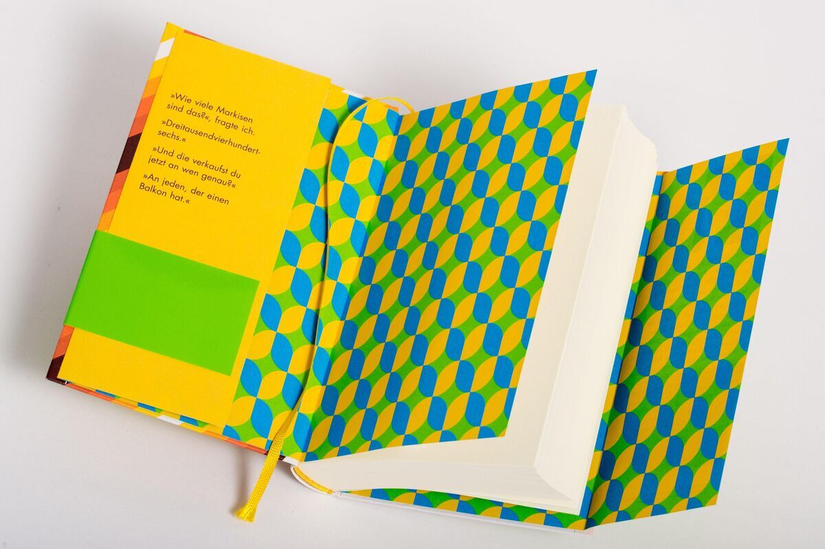 Das Bild zeigt das Buch 'Der Markisenmann' von Jan Weiler, geöffnet auf einem weißen Hintergrund. Das Buch hat ein buntes Cover mit grünen, gelben und blauen geometrischen Mustern. Ein Lesezeichen ist im Buch sichtbar.