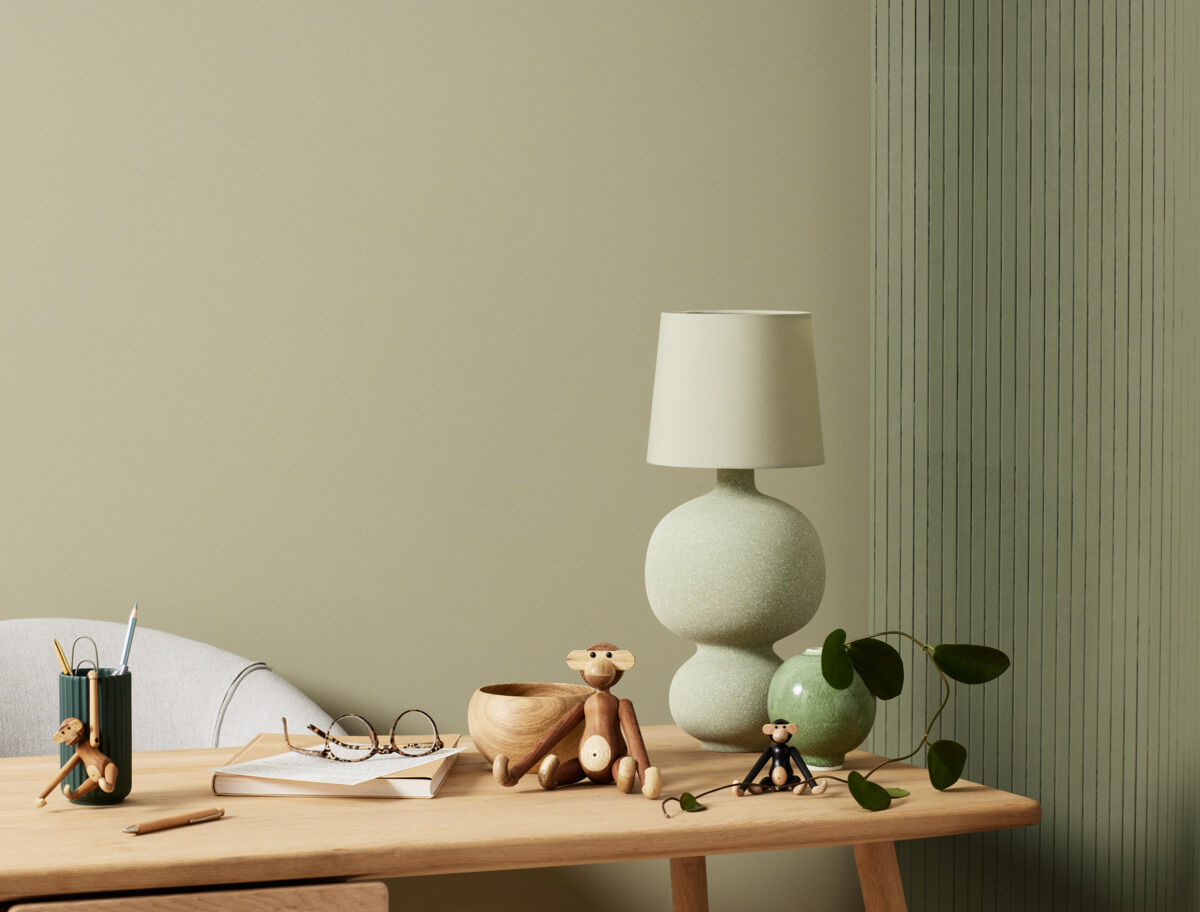 Ein stilvoller Schreibtisch mit einer Holzfigur von Kay Bojesen in Form eines Affen. Umgeben von einer Designer-Lampe, Schreibtischutensilien und weiterem dekorativen Zubehör.