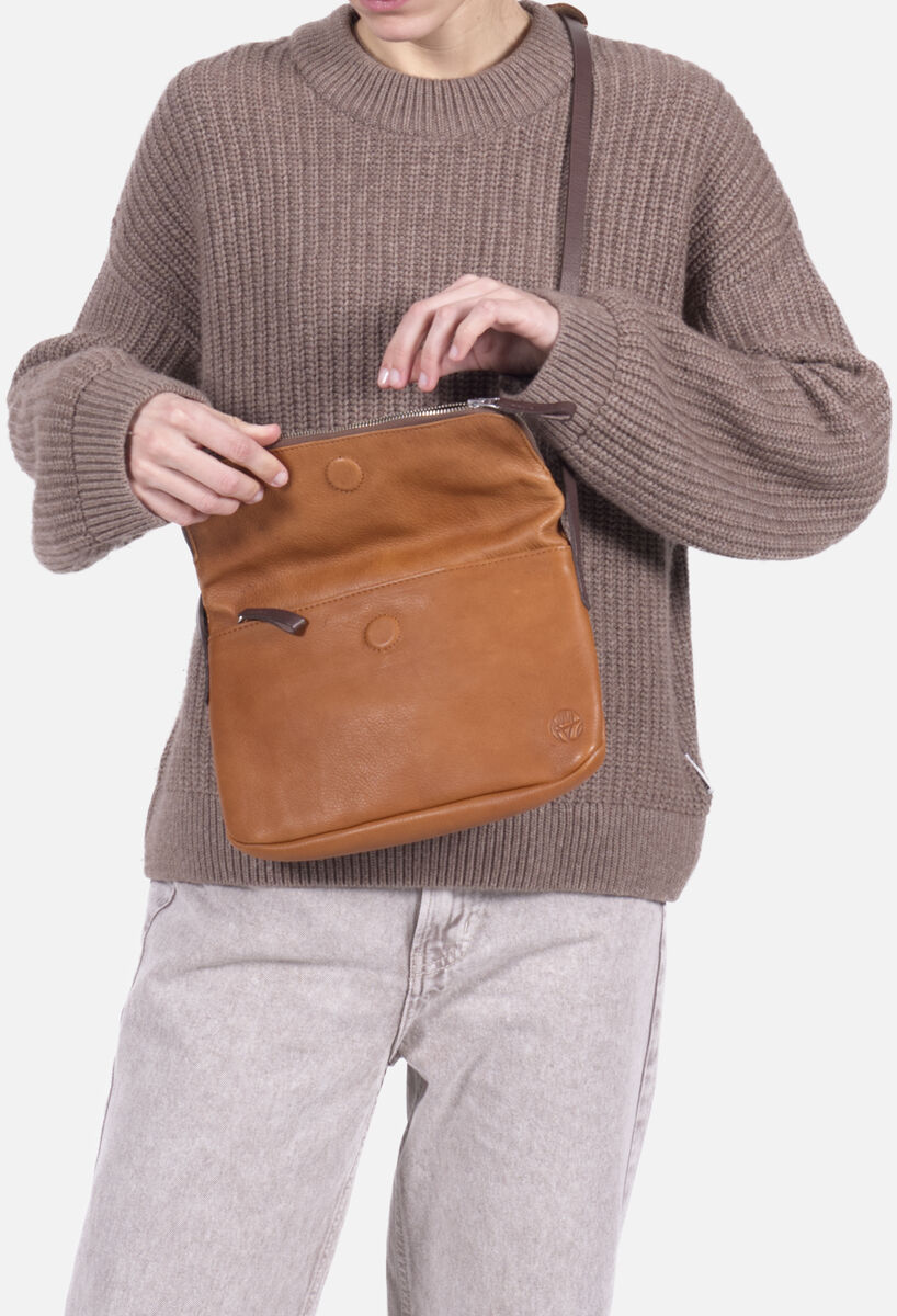 Eine Person trägt eine braune Chaza Twoway Handtasche aus Leder über der Schulter. Die Tasche hat eine schlichte, elegante Optik mit Frontreißverschluss und wird zu einem lockeren, beigen Strickpullover und hellen Jeans kombiniert. Der Hintergrund ist neutral weiß.
