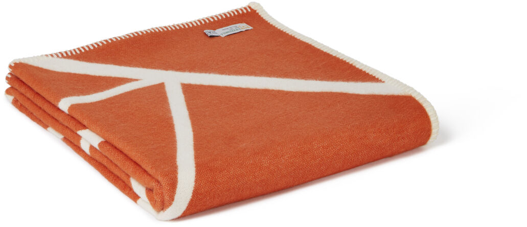 Eine zusammengefaltete Baumwolldecke in Zimtrot mit weißen Zweige-Mustern.