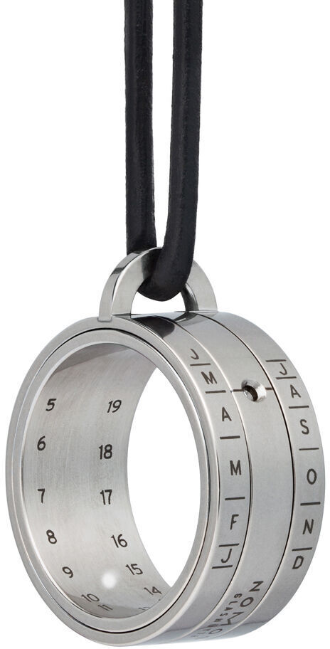 Ein silberner Edelstahlanhänger von NOMOS Glashütte in Form einer Sonnenuhr, aufgehängt an einer schwarzen Schnur.