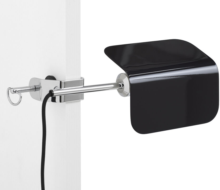 Eine moderne Lampe mit schwarzem Schirm und silbernem Befestigungsclip, der an einem weißen Brett befestigt ist. Ein Kabel führt von der Lampe weg.