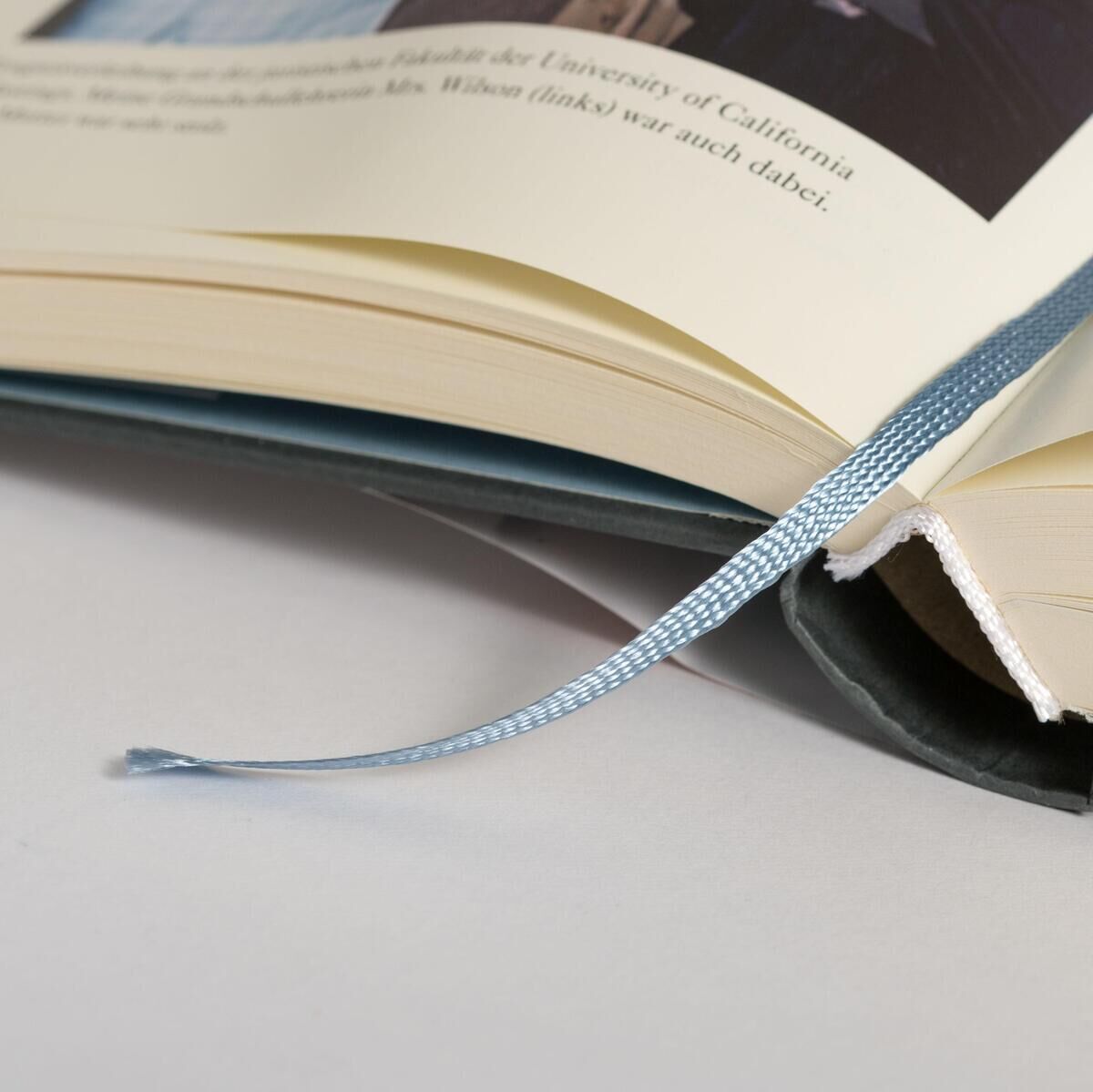 Nahaufnahme eines aufgeschlagenen Buches mit einem hellblauen Lesebändchen. Der Buchtitel scheint 'Harris, K: Wahrheit verpflichtet' zu sein. Seiten sind in einem sanften Gelbton dargestellt.