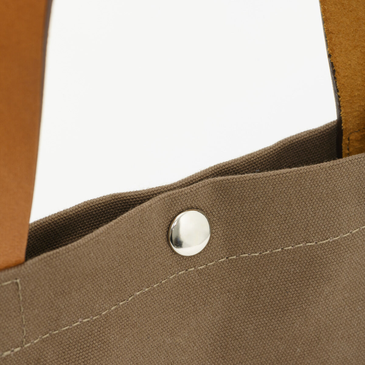 Detailaufnahme der ZEIT Shop Jubiläums-Shopper Baumwolltasche in Beige mit einem hellbraunen Griff und einer silbernen Niete.