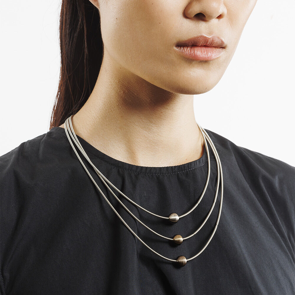 Eine stilvolle Halskette namens 'Collier »Planet«' mit drei silbernen Metallkugeln, getragen von einer Frau in einem schwarzen Oberteil. Das Design ist minimalistisch und elegant.