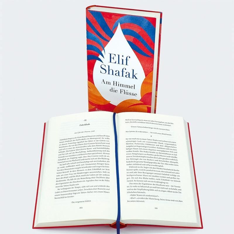 Das Bild zeigt das Buch 'Am Himmel die Flüsse' von Elif Shafak. Das Buch hat ein auffälliges Cover in Blau, Rot und Orange. Vor dem geschlossenen Buch liegt ein geöffnetes Exemplar des Romans, das mit einem blauen Lesebändchen versehen ist.