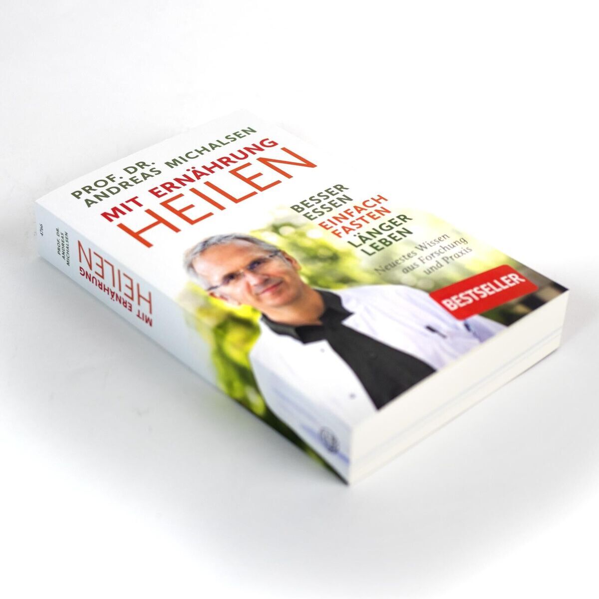Das Bild zeigt das Buch 'Mit Ernährung heilen' von Prof. Dr. Andreas Michalsen. Es liegt auf einer weißen Oberfläche und ist schräg fotografiert, sodass der Einband und das Cover gut sichtbar sind. Auf dem Cover befindet sich ein Bild von Prof. Michalsen sowie der Titel des Buches. Der Titel und Untertitel sind in roten und schwarzen Buchstaben geschrieben. Ein Aufkleber mit der Aufschrift 'Bestseller' ist in der unteren rechten Ecke des Buches zu sehen.