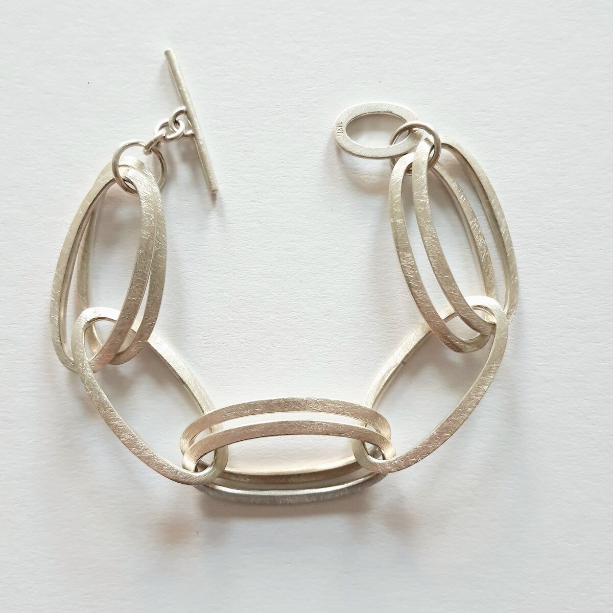 Ein elegantes Armband mit mehreren ineinander verschlungenen silbernen Gliedern auf einem weißen Hintergrund. Dieses minimalistische und stilvolle Schmuckstück eignet sich perfekt als Geschenk für Frauen zu verschiedenen Anlässen wie Weihnachten, Valentinstag, Geburtstagen und Hochzeiten.